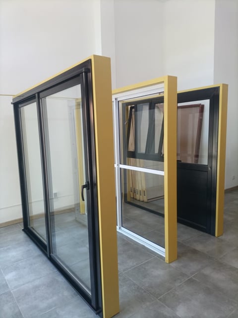 Three sliding door and window samples with gold and black frames displayed on a concrete floor in a showroom