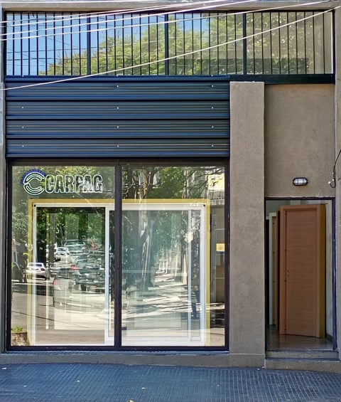 Modern storefront with CARPAC signage, large windows, blue horizontal panels above, and brown entry door on the side.